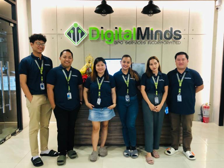 Six people stand in a row wearing matching blue shirts and name badges in front of a sign that reads "Digital Minds BPO Services Incorporated," showcasing the professionalism typical of top-tier outsourcing companies in the Philippines.