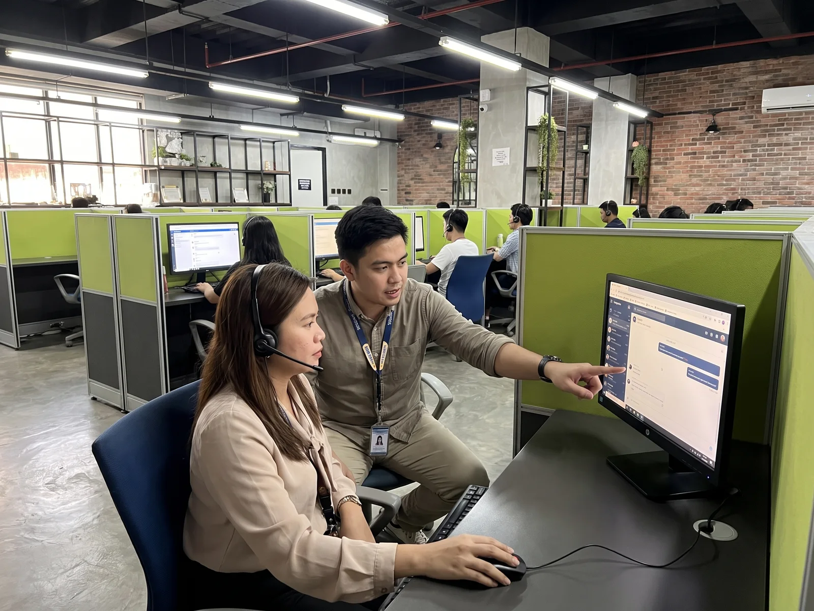 A team leader coaches a chat agent at her workstation in a Naga City office