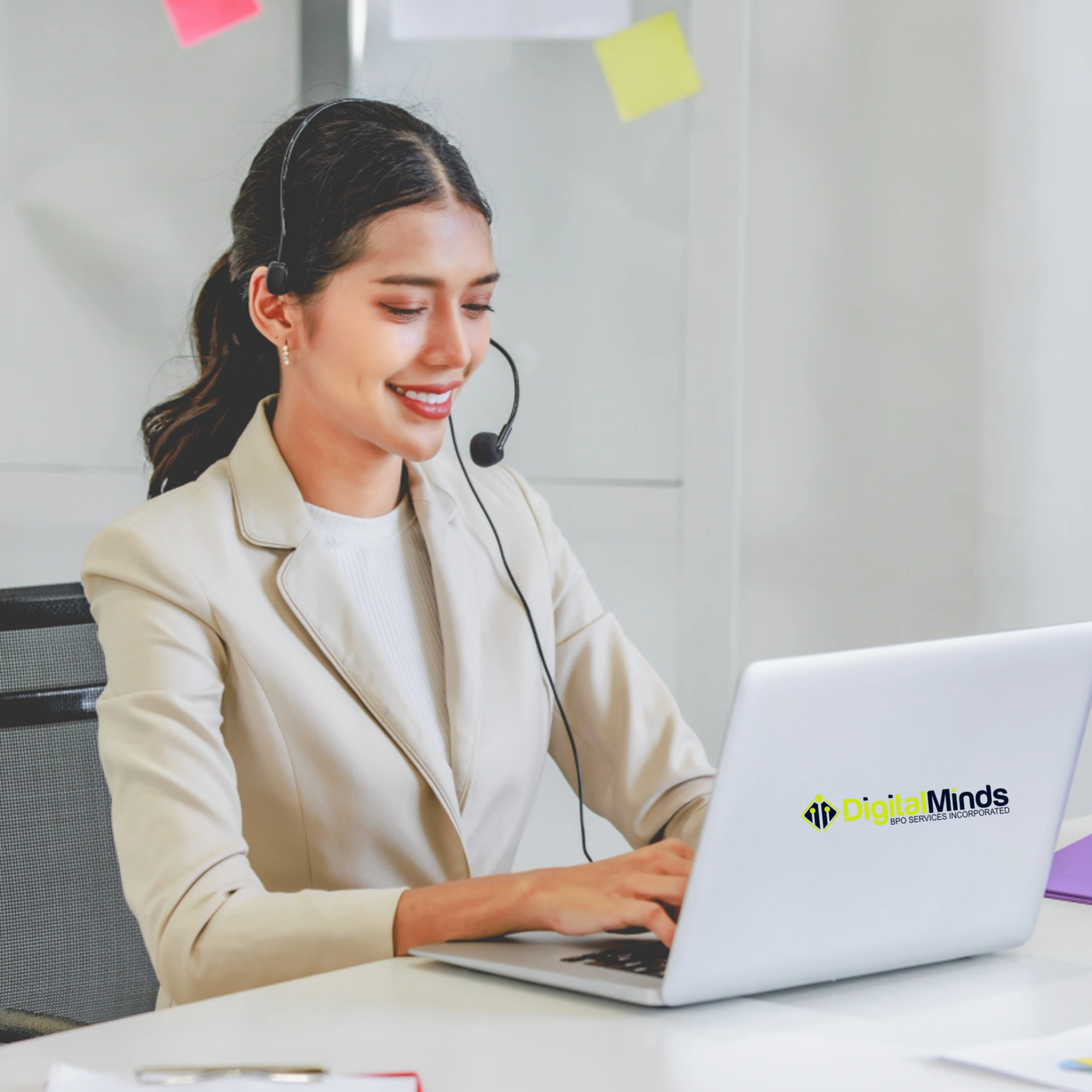 A woman wearing a headset sits at a desk, typing on a laptop with a "Digital Minds" logo, representing live chat outsourcing Philippines as she conducts customer service or a virtual meeting. A woman wearing a headset sits at a desk, typing on a laptop with a "Digital Minds" logo, representing live chat outsourcing Philippines as she conducts customer service or a virtual meeting.